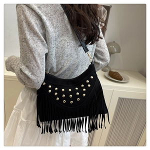 Detail of black suede shoulder bag with gold studs and long fringe tassels on model
