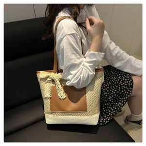 Close-up of woven straw tote bag featuring a beige lace bow and brown leather pocket detail