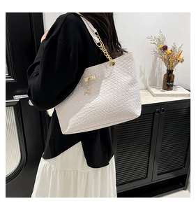 Close-up of white woven tote bag featuring gold chain strap and deer pendant detail