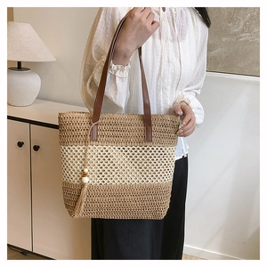 Detalle del bolso tote de paja tejida con asas de cuero marrón y borlas de cuentas de madera