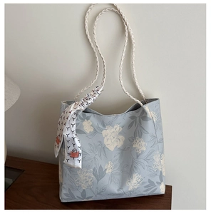 Detail of light blue floral canvas tote bag featuring woven straps and decorative silk scarf