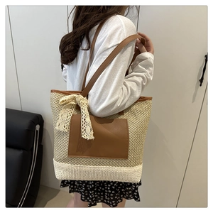 Detail of hand-woven straw tote bag with brown leather pocket and white lace bow