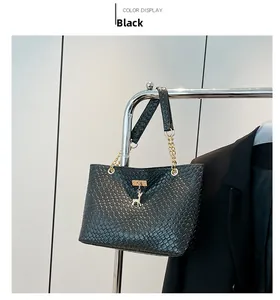Detail of black woven texture handbag with golden deer charm and metallic chain strap