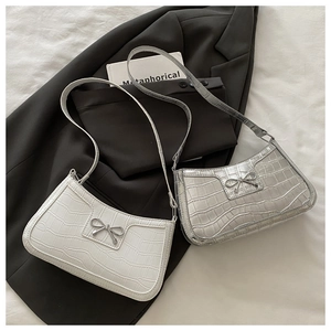 Flat lay of crocodile pattern mini shoulder bags with metallic bow detail on dark blazer