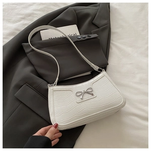 Detail of white crocodile texture hobo bag featuring a metal bow accent on a blazer