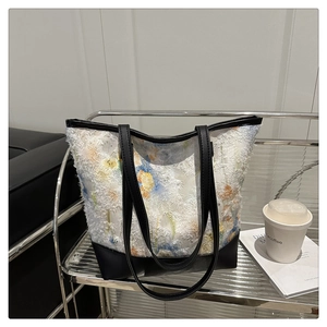 Detail view of floral embroidered chiffon tote bag with black leather base on a shelf