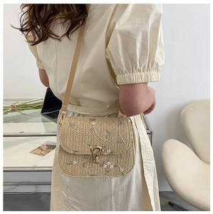 Detail of hand-woven straw crossbody bag featuring delicate pink floral embroidery and metal lock