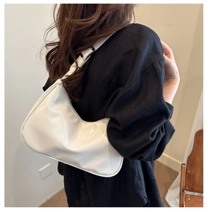 Close-up of a glossy white hobo bag worn on shoulder over a black blazer for chic style