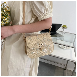 Close-up of beige straw woven bag with pink flower embroidery and metal buckle