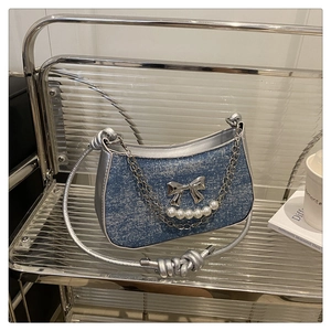 Détail du sac hobo en denim bleu avec nœud métallique argenté et décor de chaîne perle