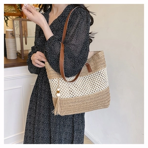 Detail of striped straw tote bag featuring brown leather handles and decorative tassel
