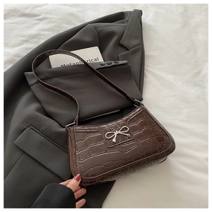 Detailed view of dark brown crocodile embossed texture with silver bow buckle on bag