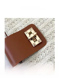 Close-up of textured gold metal buckle and brown leather flap on woven tote bag