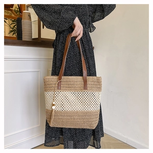 Detailed macro view of woven straw tote bag with leather handles and tassel charm