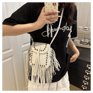 Detailed view of white faux leather crossbody bag with metal rivets and long fringe tassels