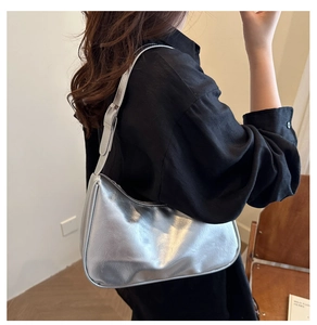 Silver crescent underarm bag with pleated metallic texture shown on shoulder