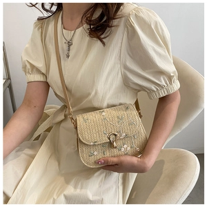 Detail of floral embroidery on a handwoven straw crossbody bag with golden metal twist lock