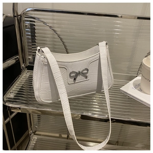 Close-up of white crocodile pattern bag featuring a silver metal bow and moon shape