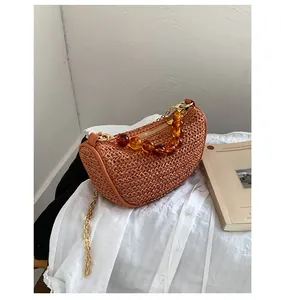 Detail of hand-woven straw crossbody bag featuring amber bead chain and golden strap