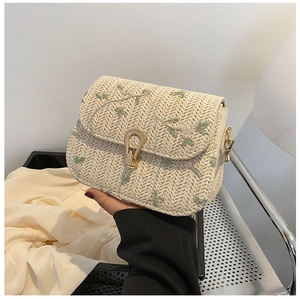 Detail of floral embroidery and gold horseshoe lock on beige straw crossbody bag
