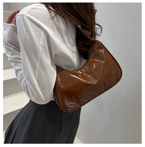 Close-up of a brown glossy patent leather crescent shoulder bag worn with minimalist white outfit