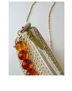 Detail of cream straw shoulder bag featuring golden chain and amber bead pendant