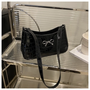 Detailed close-up of glossy crocodile pattern on black shoulder bag with silver bow detail