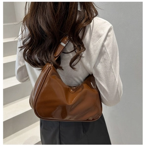 Rear view of model wearing a brown glossy crescent hobo bag with silver buckle on stairs
