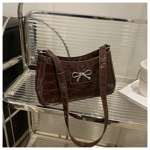 Detail of dark brown crocodile embossed leather with silver bow buckle on handbag