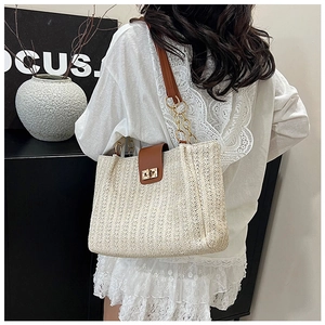 Detail of woven tote bag featuring brown leather strap and golden metal chain link