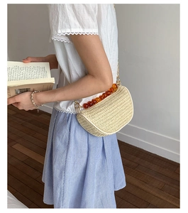 Detail of straw woven half-moon bag featuring orange resin beads and gold chain strap