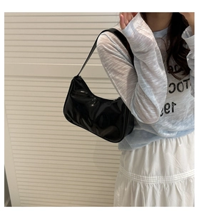 Close-up of a glossy black patent leather crescent shoulder bag worn on the arm