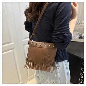 Sac seau marron à franges avec clous argentés porté en bandoulière pour un look rétro