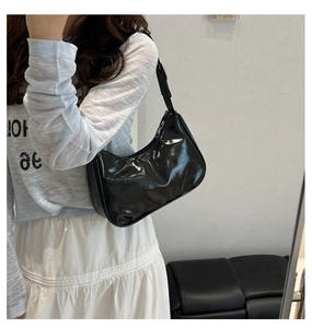 Detail of glossy patent leather half-moon bag featuring silver zipper and adjustable strap