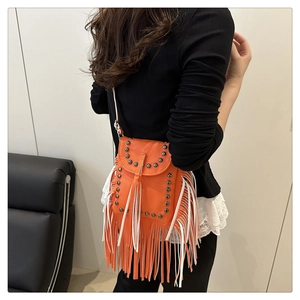 Close-up of orange tassel crossbody bag with dark grey metal studs on pebbled leather