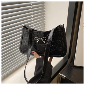 Detail of black faux crocodile leather shoulder bag featuring a silver metal bow accent