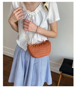 Detail view of woven terracotta crescent bag with amber acrylic handle and gold chain strap