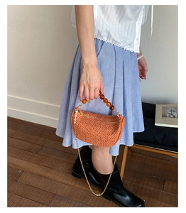 Close-up of orange woven bag with brown beaded handle and gold metal chain strap