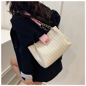Close-up of woven straw tote bag featuring pink leather straps and gold metal chain buckle