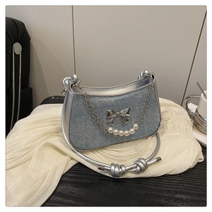 Détail du sac à main en cuir argenté et denim bleu avec chaîne en perles et nœud décoratif