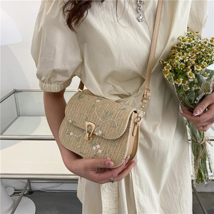 Beige straw crossbody bag with floral embroidery and golden horseshoe lock worn by model