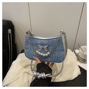Détail d'un sac en denim bleu avec anse argentée nouée et chaîne métallique décorative