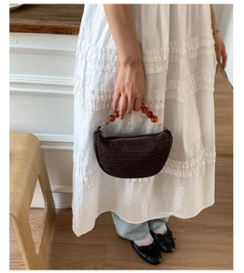 Detail of dark brown woven crescent bag with amber resin bead handle and metal zipper