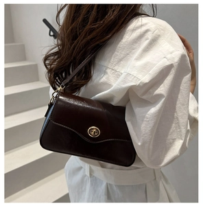 Détail du sac sous le bras en cuir brillant marron foncé avec fermoir rotatif doré et bandoulière