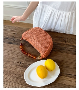 Detail of orange woven straw hobo bag with amber beaded handle on wooden background