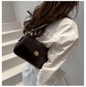 Détail d'un sac à bandoulière en cuir brillant marron foncé avec un fermoir doré circulaire