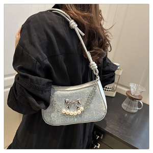 Détail du sac en denim bleu clair avec nœud argenté, chaîne de perles et bandoulière nouée