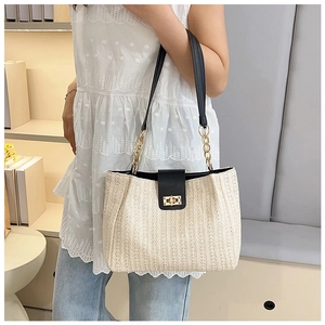 Detail of woven tote bag showing cream straw texture, black leather straps and gold lock