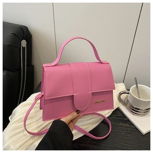 Détail d'un petit sac carré rose avec fermeture à rabat, logo en métal et bandoulière