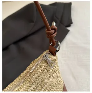 Détail d'un sac en paille tissée avec fermeture éclair argentée et bandoulière en cuir brun